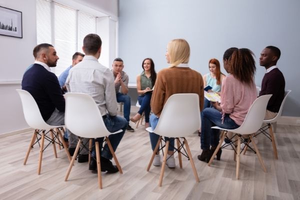 an image of group of individuals gathered around sitting in a circle with chairs having a discussion.