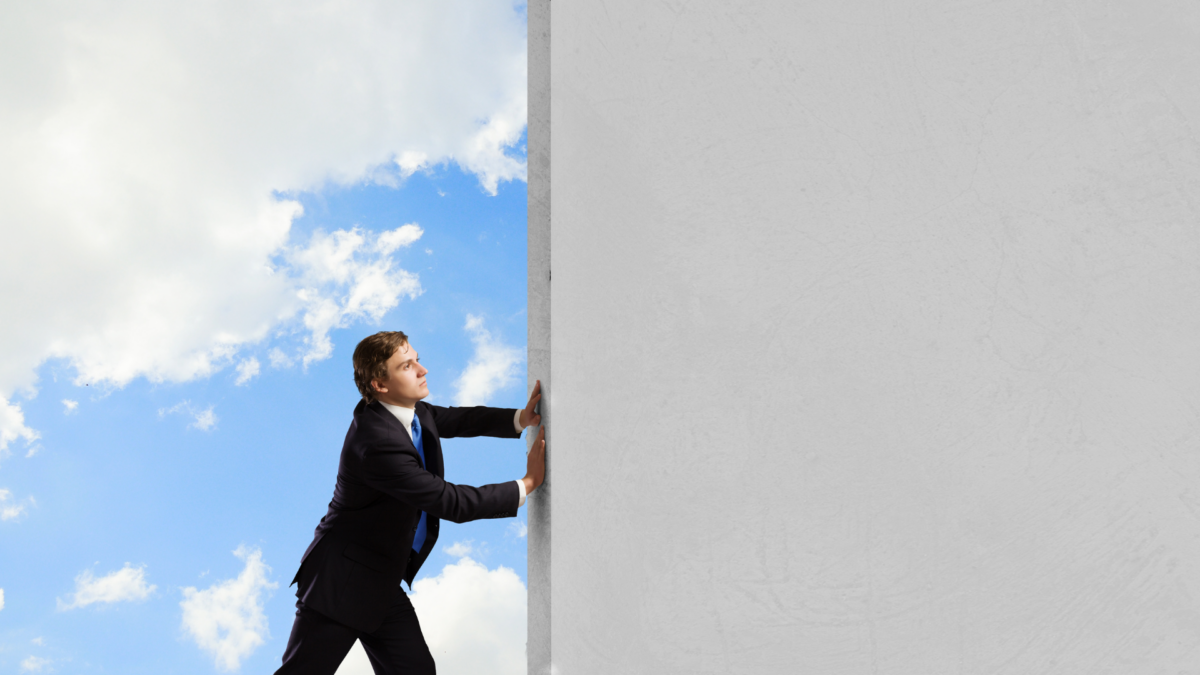 a man pushing a wall on a sky blue background.