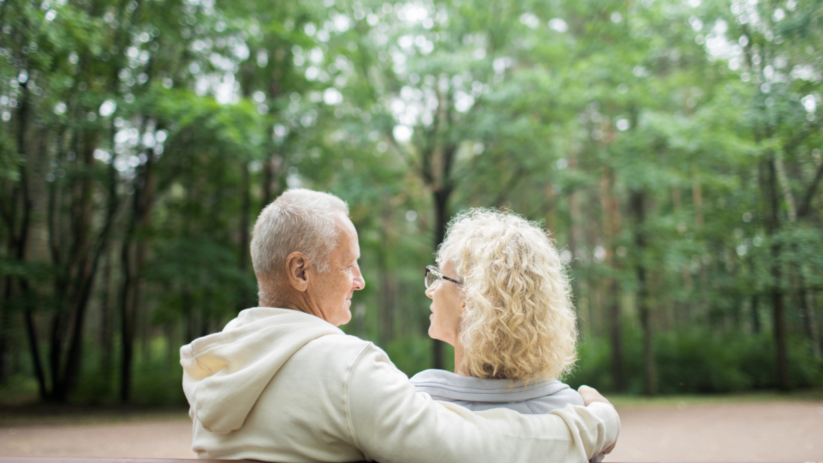 an image of an elderly couple sitting on the bench with the background of green trees.